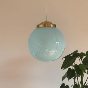 May include: A light blue glass globe pendant light with a gold metal fixture. The light is hanging from a white cord.