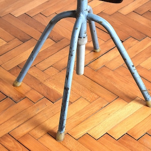 Puede incluir: Un soporte de metal azul de tres patas con una parte superior redonda. El soporte est&aacute; sobre un suelo de madera.