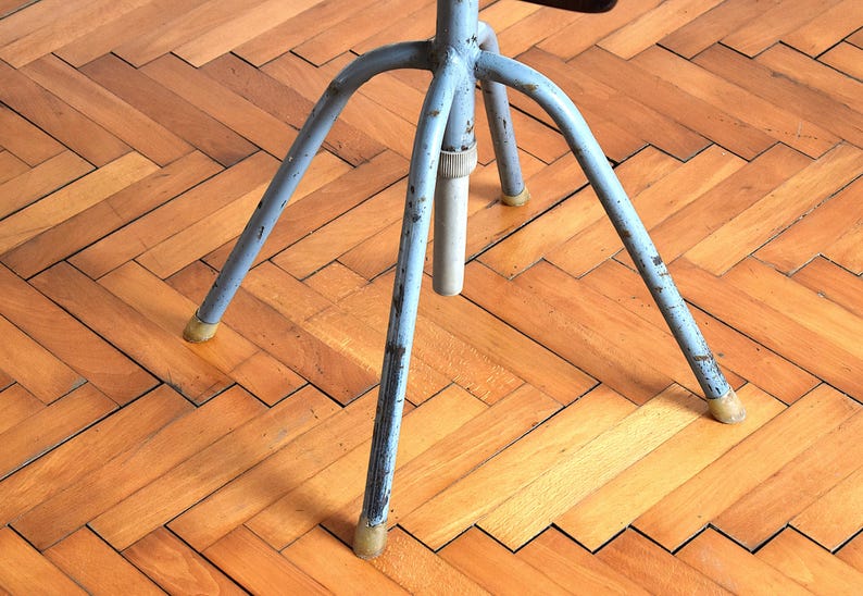 Puede incluir: Un soporte de metal azul de tres patas con una parte superior redonda. El soporte est&aacute; sobre un suelo de madera.