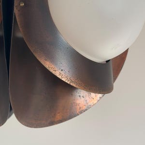 Puede incluir: Primer plano de una l&aacute;mpara colgante de metal de color cobre con una pantalla de globo blanco. La l&aacute;mpara tiene un dise&ntilde;o en capas y org&aacute;nico.