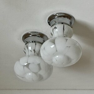 May include: Two ceiling-mounted light fixtures. Each fixture has a chrome base and a white glass shade with a marbled pattern. The shades are round and bulbous, with a smaller, cylindrical section above.