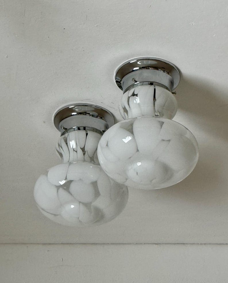May include: Two ceiling-mounted light fixtures. Each fixture has a chrome base and a white glass shade with a marbled pattern. The shades are round and bulbous, with a smaller, cylindrical section above.