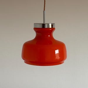 May include: A bright orange glass pendant light with a chrome finish. The light is suspended from a brown cord.