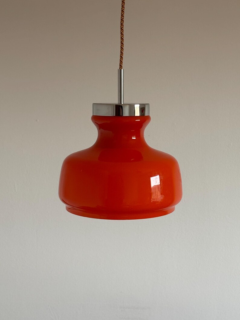 May include: A bright orange glass pendant light with a chrome finish. The light is suspended from a brown cord.