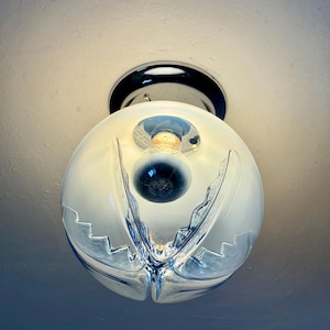 May include: A contemporary ceiling light. The spherical, frosted glass shade features a distinctive, abstract design with blue detailing. The light is mounted on a chrome base, offering a sleek, modern aesthetic.