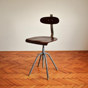 Puede incluir: Una silla giratoria industrial vintage con un asiento de madera marr&oacute;n oscuro y una base de metal azul. La silla tiene un dise&ntilde;o simple y funcional y est&aacute; en buen estado.