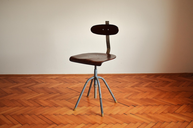 Puede incluir: Una silla giratoria industrial vintage con un asiento de madera marr&oacute;n oscuro y una base de metal azul. La silla tiene un dise&ntilde;o simple y funcional y est&aacute; en buen estado.