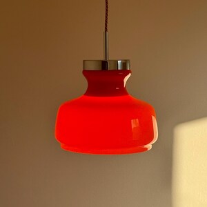 May include: A red glass pendant light with a chrome finish. The light is hanging from a red cord.