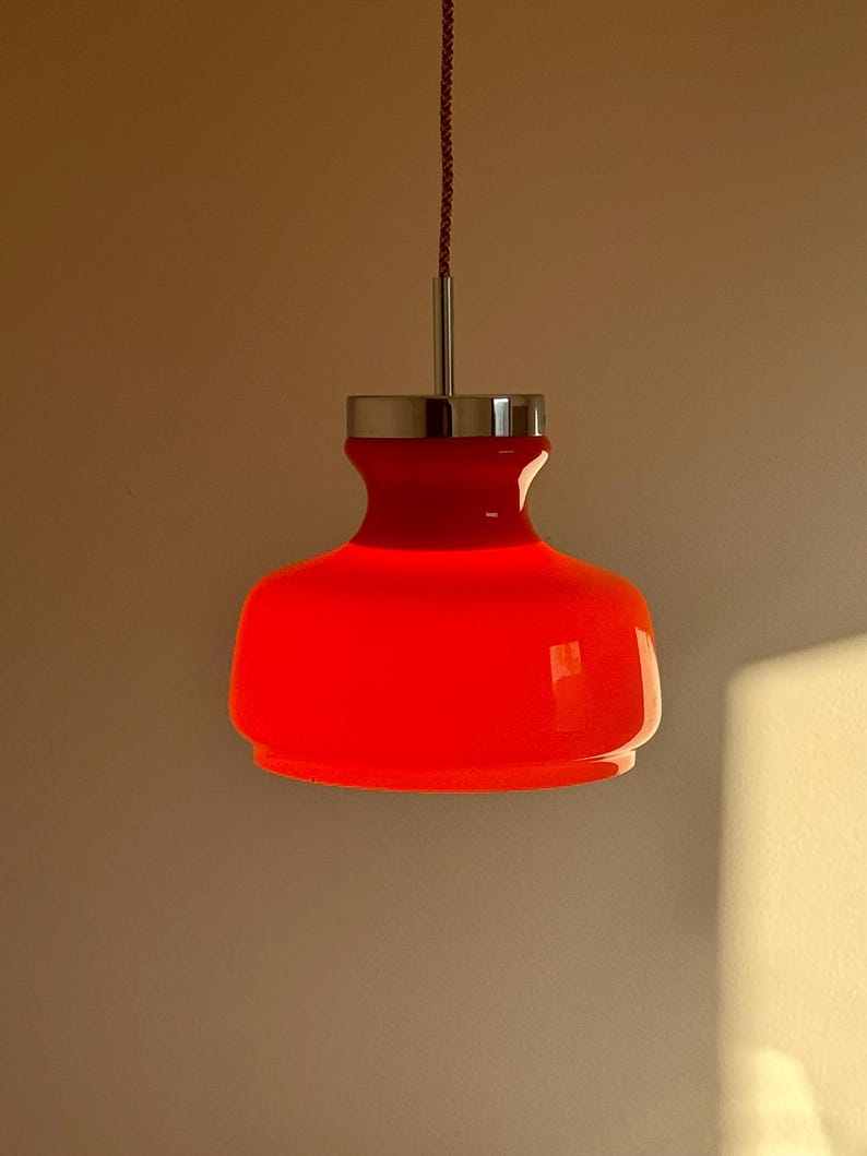May include: A red glass pendant light with a chrome finish. The light is hanging from a red cord.
