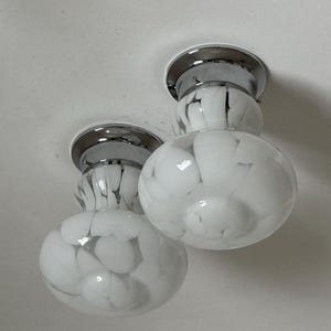 May include: Two ceiling-mounted light fixtures. Each fixture has a chrome base and a white glass globe with a marbled pattern of gray and white. The globes are round and bulbous, with a smaller, cylindrical section connecting them to the base.