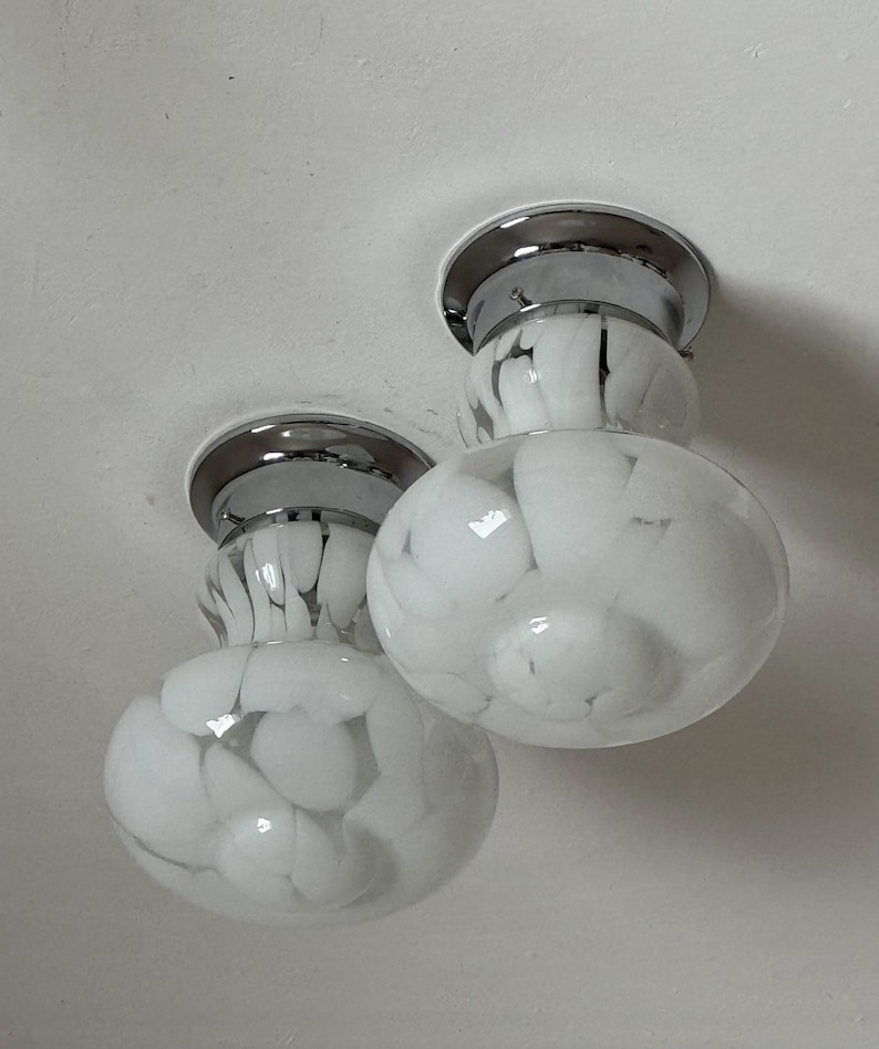 May include: Two ceiling-mounted light fixtures. Each fixture has a chrome base and a white glass globe with a marbled pattern of gray and white. The globes are round and bulbous, with a smaller, cylindrical section connecting them to the base.