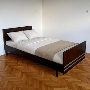 May include: A dark brown bed with a headboard and footboard, featuring a white blanket and two pillows. A beige throw blanket is at the foot of the bed. The bed is on a wooden floor.