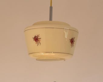 May include: Cream-colored pendant light with red floral accents. The light fixture has a rounded, bowl-like shape with a thin, dark red band around the top and bottom. The light hangs from a yellow cord and a silver metal rod.