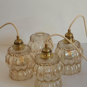 May include: Four clear glass pendant lights with a textured, ribbed design and gold metal accents. The lights are hanging from white cords.