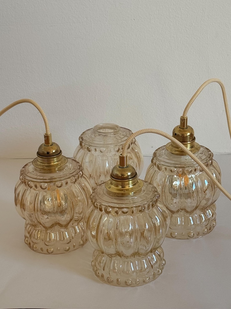May include: Four clear glass pendant lights with a textured, ribbed design and gold metal accents. The lights are hanging from white cords.