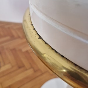 May include: A white table with a gold metal trim around the top. The table has a round top and a single pedestal base.