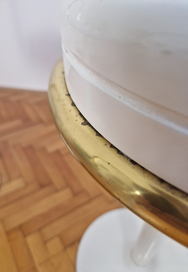 May include: A white table with a gold metal trim around the top. The table has a round top and a single pedestal base.
