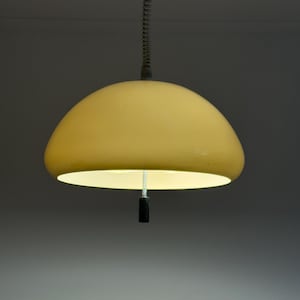 May include: A hanging, yellow, dome-shaped pendant light fixture. The light has a black pull cord and a metal chain. The light is suspended from the ceiling and is illuminated from within, casting a warm glow.