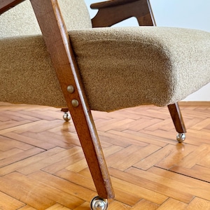 May include: A brown wooden armchair with a beige fabric upholstery and four metal wheels. The chair has a simple, mid-century modern design.
