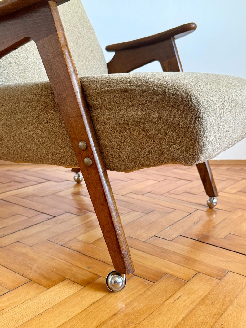 May include: A brown wooden armchair with a beige fabric upholstery and four metal wheels. The chair has a simple, mid-century modern design.