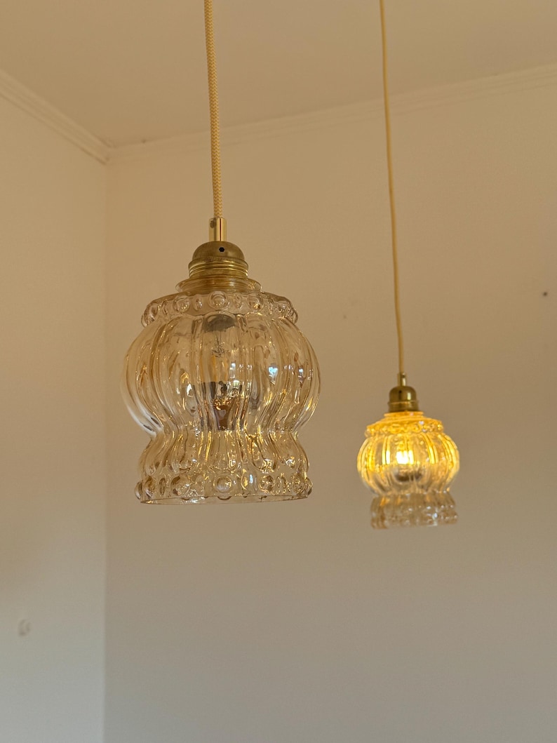 May include: Two gold pendant lights with clear glass shades. The shades have a textured, ribbed design.