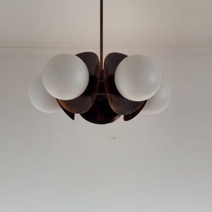 May include: A brown, wooden, flower-shaped chandelier with five white globe light bulbs.