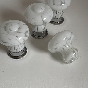 May include: Four white and gray glass mushroom-shaped cabinet knobs with chrome bases. One knob is lying on its side. The knobs have a speckled pattern and are designed for furniture or decorative use.
