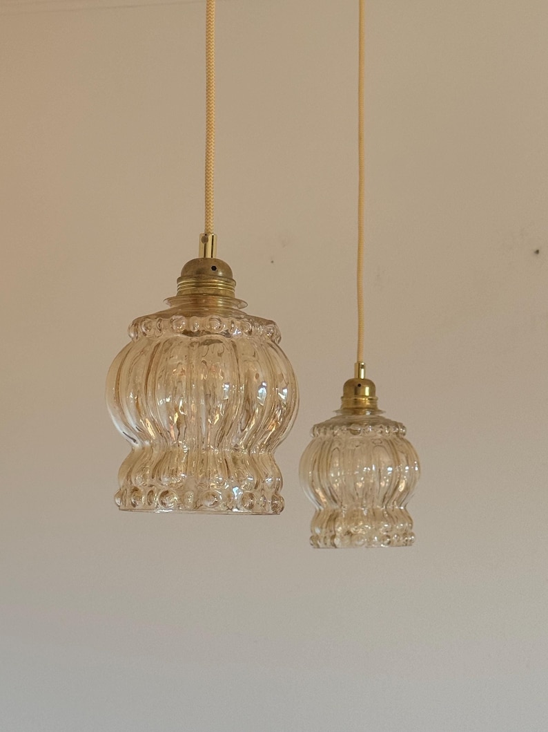 May include: Two clear glass pendant lights with a ribbed texture and a gold metal finish. The lights are hanging from a white cord.