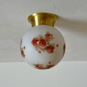 May include: A round, white glass ceiling light fixture with a brass-colored base. The globe is decorated with clusters of red and orange roses. The fixture is mounted on a white ceiling.