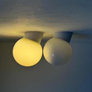 May include: Two modern ceiling lights with spherical, frosted glass shades. One is illuminated with a warm yellow glow, while the other is unlit. The lights are mounted on a gray base.