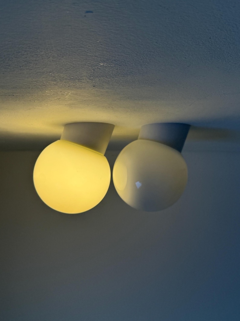 May include: Two modern ceiling lights with spherical, frosted glass shades. One is illuminated with a warm yellow glow, while the other is unlit. The lights are mounted on a gray base.