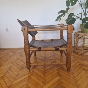 May include: A brown leather and wood chair with a simple design. The chair has a wide, flat seat and a low back. The chair is made of natural materials and has a rustic look.