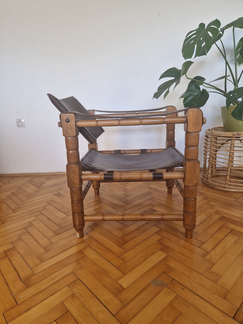 May include: A brown leather and wood chair with a simple design. The chair has a wide, flat seat and a low back. The chair is made of natural materials and has a rustic look.