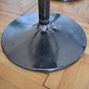 Op de afbeelding: Een zwarte metalen basis met een ronde, gladde bovenkant. De basis heeft een glanzend, reflecterend oppervlak.