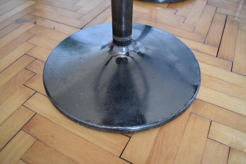 Op de afbeelding: Een zwarte metalen basis met een ronde, gladde bovenkant. De basis heeft een glanzend, reflecterend oppervlak.
