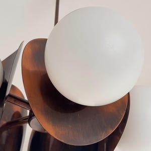 May include: A copper-toned chandelier with multiple white globe light fixtures. The chandelier has a unique design with overlapping, curved, copper-toned plates.