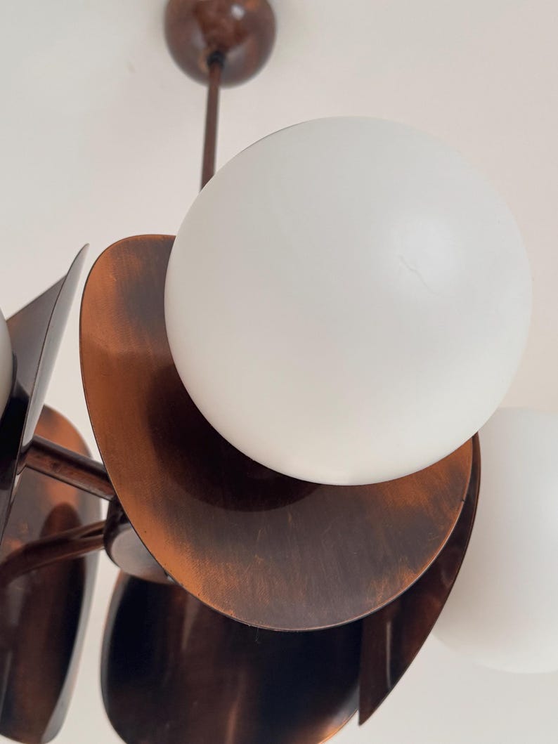 May include: A copper-toned chandelier with multiple white globe light fixtures. The chandelier has a unique design with overlapping, curved, copper-toned plates.