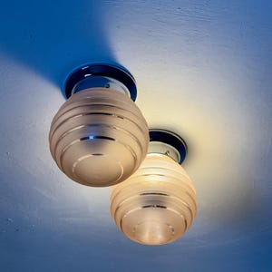 May include: Two ceiling-mounted light fixtures with frosted glass globes. Each globe has horizontal etched lines and is mounted on a chrome base with a dark blue accent. The lights are illuminated, casting a warm glow.
