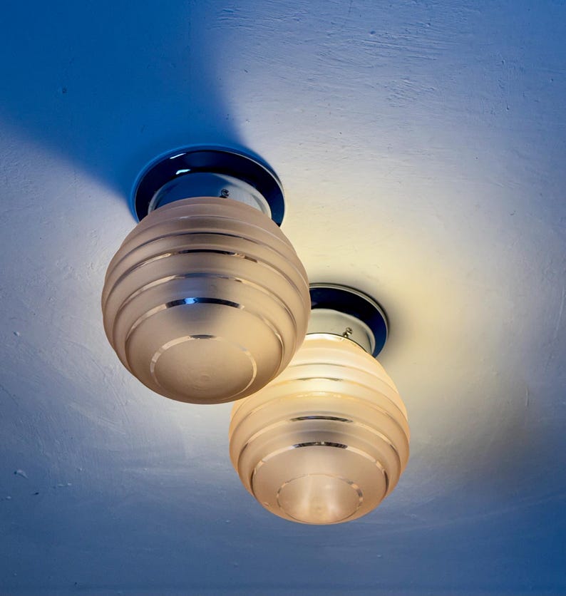May include: Two ceiling-mounted light fixtures with frosted glass globes. Each globe has horizontal etched lines and is mounted on a chrome base with a dark blue accent. The lights are illuminated, casting a warm glow.