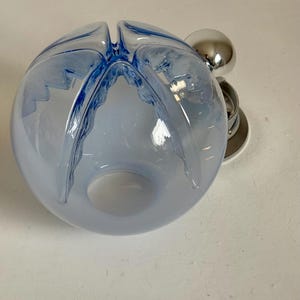 May include: A light blue glass bowl with a unique design. The bowl has a spherical shape with four curved openings at the top. A chrome-coloured metal accent is attached to the side.