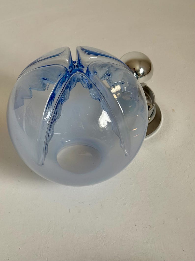 May include: A light blue glass bowl with a unique design. The bowl has a spherical shape with four curved openings at the top. A chrome-coloured metal accent is attached to the side.