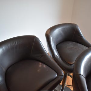 Op de afbeelding: Vier bruine leren barstoelen met een gebogen rugleuning en een ronde zitting.