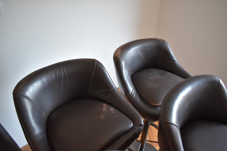 Op de afbeelding: Vier bruine leren barstoelen met een gebogen rugleuning en een ronde zitting.