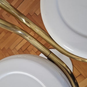 May include: Two white round stools with gold metal frames. The stools are connected by the frames, which are curved and have a shiny finish.