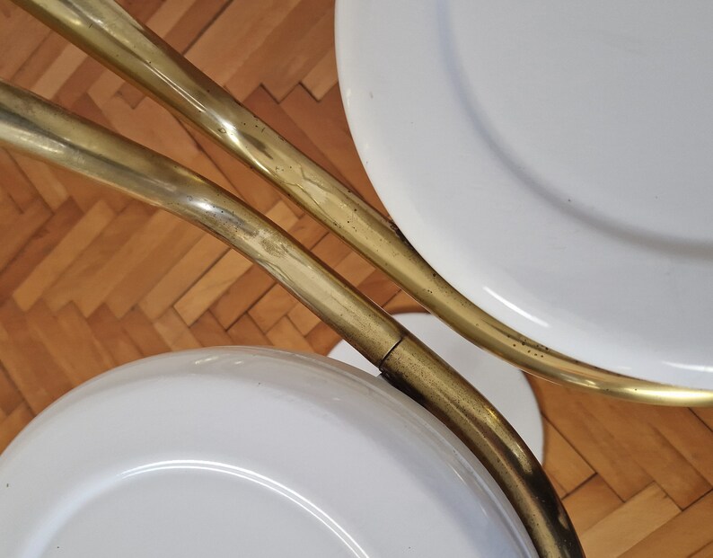 May include: Two white round stools with gold metal frames. The stools are connected by the frames, which are curved and have a shiny finish.