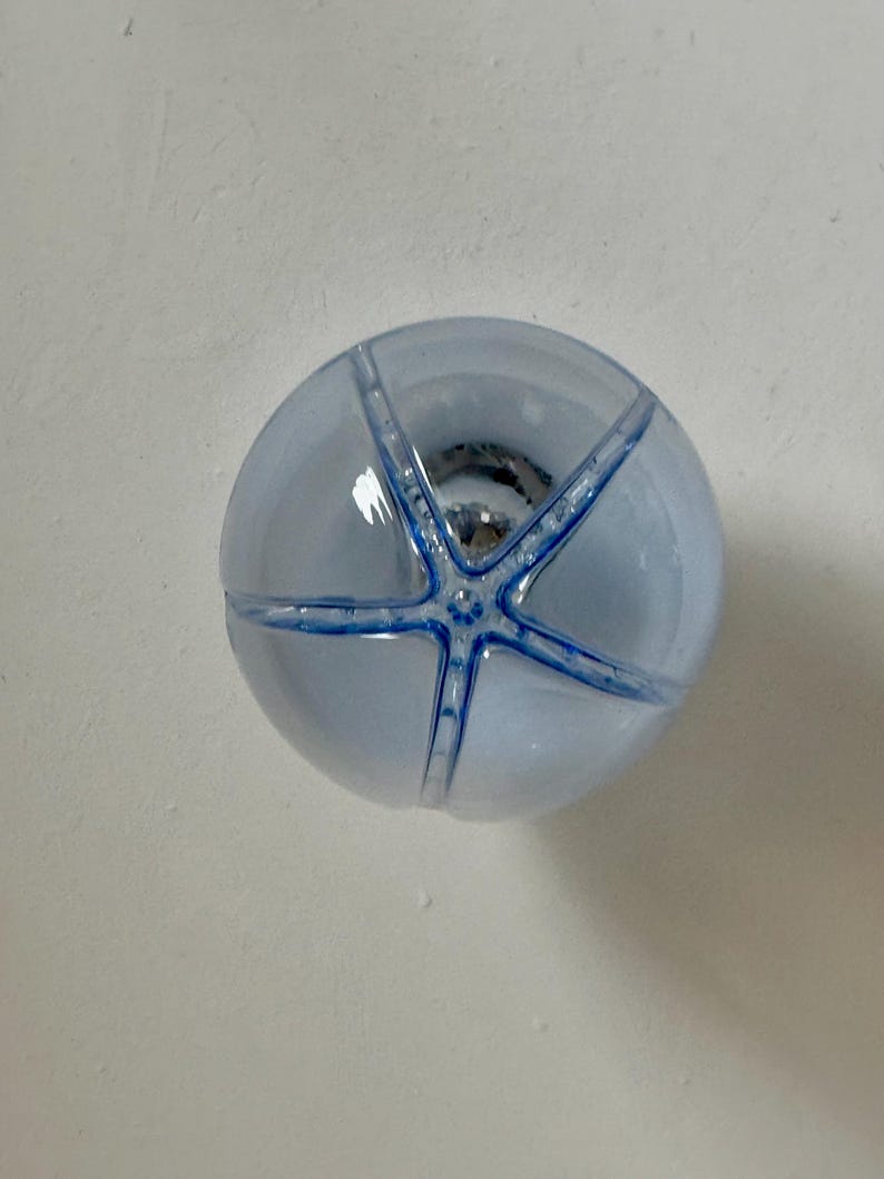 May include: A round, pale blue glass knob featuring a starfish design in a darker blue. The knob is transparent, revealing the hardware within. This decorative knob is suitable for cabinets, drawers, or furniture.