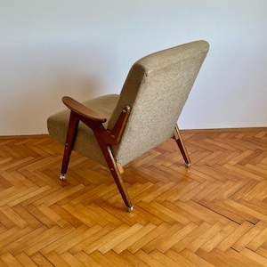May include: A brown armchair with a beige fabric upholstery and wooden legs. The chair has a curved back and armrests. The chair is sitting on a wooden floor with a herringbone pattern.