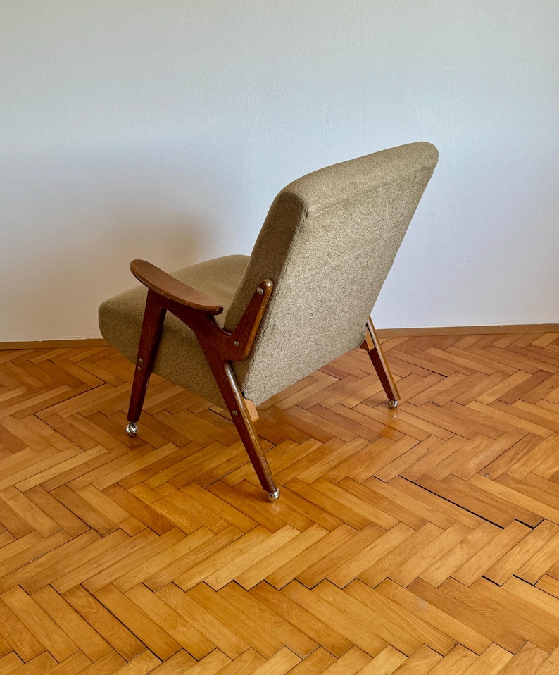 May include: A brown armchair with a beige fabric upholstery and wooden legs. The chair has a curved back and armrests. The chair is sitting on a wooden floor with a herringbone pattern.