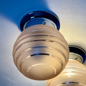 May include: Two ceiling-mounted light fixtures. Each fixture has a chrome base and a frosted glass globe with horizontal etched lines. The globes are egg-shaped. The ceiling is painted white and blue.
