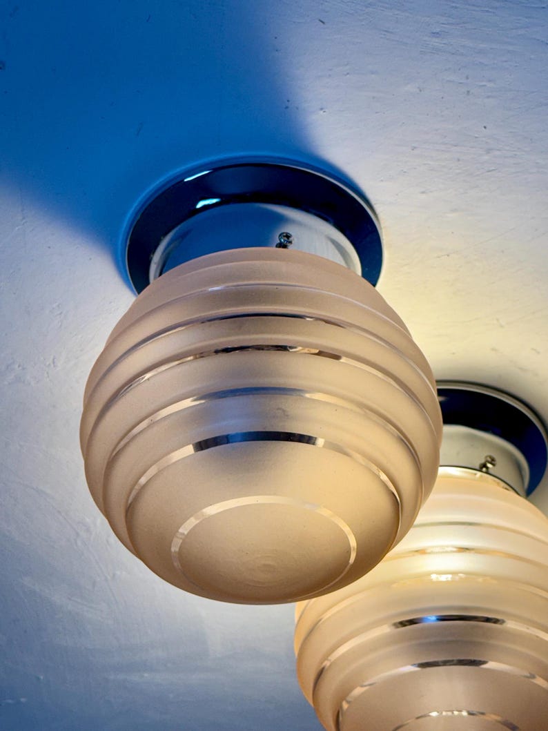 May include: Two ceiling-mounted light fixtures. Each fixture has a chrome base and a frosted glass globe with horizontal etched lines. The globes are egg-shaped. The ceiling is painted white and blue.